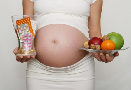 Таблетки и фрукты в руках беременной
